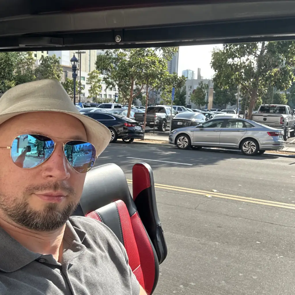 Thomas, owner of Nado Karts, standing next to a premium electric golf cart on a sunny street in Coronado, California.
