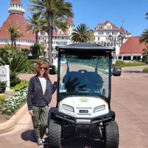 A woman standing next to a white Nado Karts golf cart in front of the historic Hotel Del Coronado.
