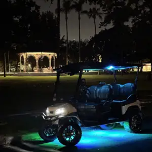 A Nado Karts golf cart with bright blue underglow parked at night near the lit-up Spreckels Park gazebo in Coronado.