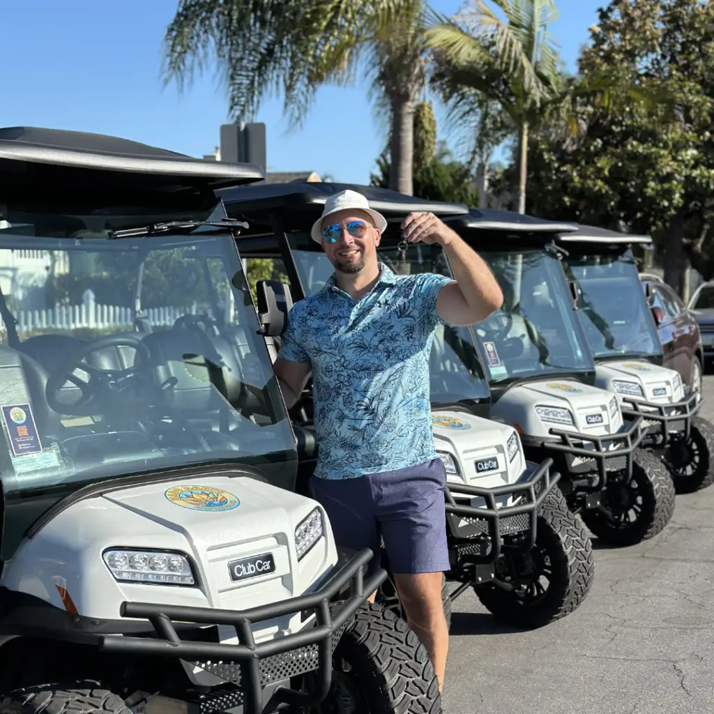 Thomas, owner of Nado Karts, smiling and holding keys next to a fleet of premium white Club Car electric golf carts in Coronado, California.