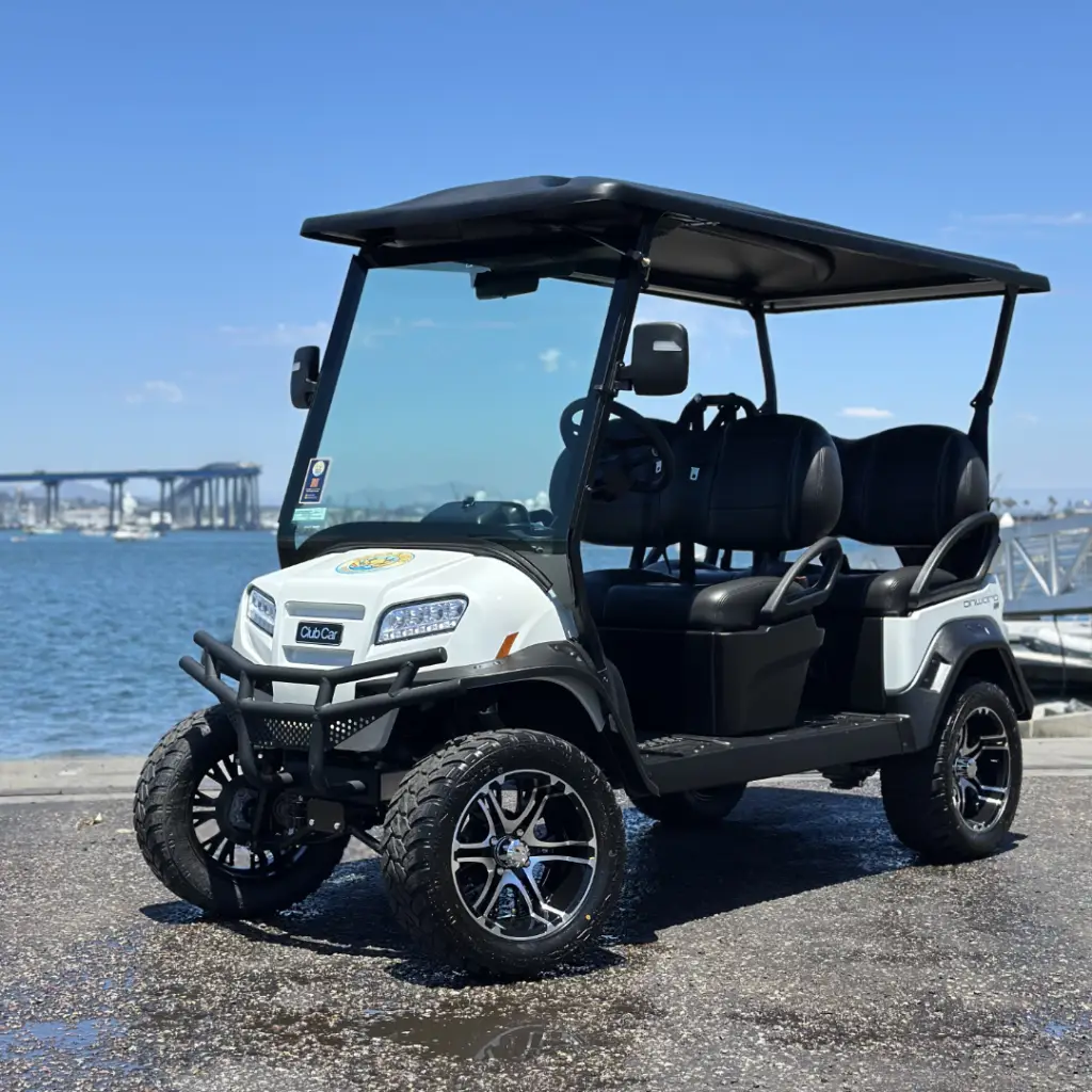 A premium white Nado Karts electric golf cart parked near the water with the Coronado Bridge in the background.